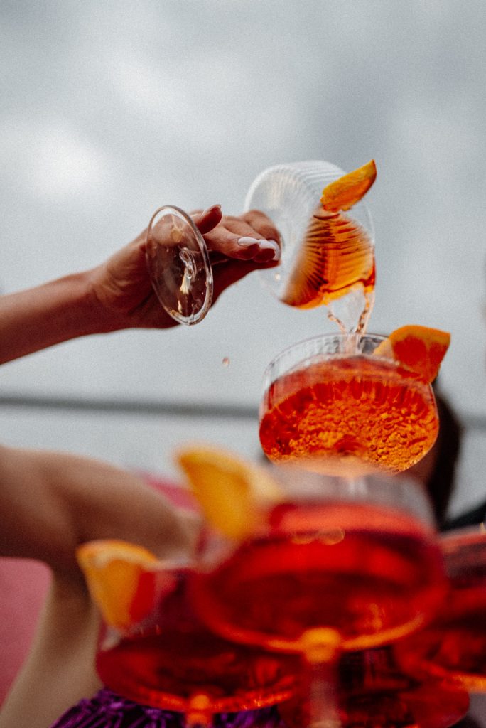 Narancsszelettel díszített aperitifek koccintás közben, felhős ég előtt